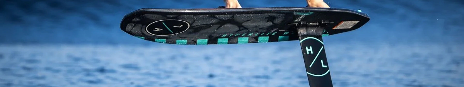 A person rides a black hydrofoil surfboard, which hovers above the blue water, with only the foil submerged.