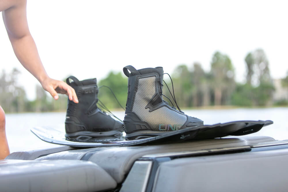 A man showcasing the high-response of a heat moldable Ronix 2024 One Carbitex Boot while balancing gracefully on top of a wakeboard.