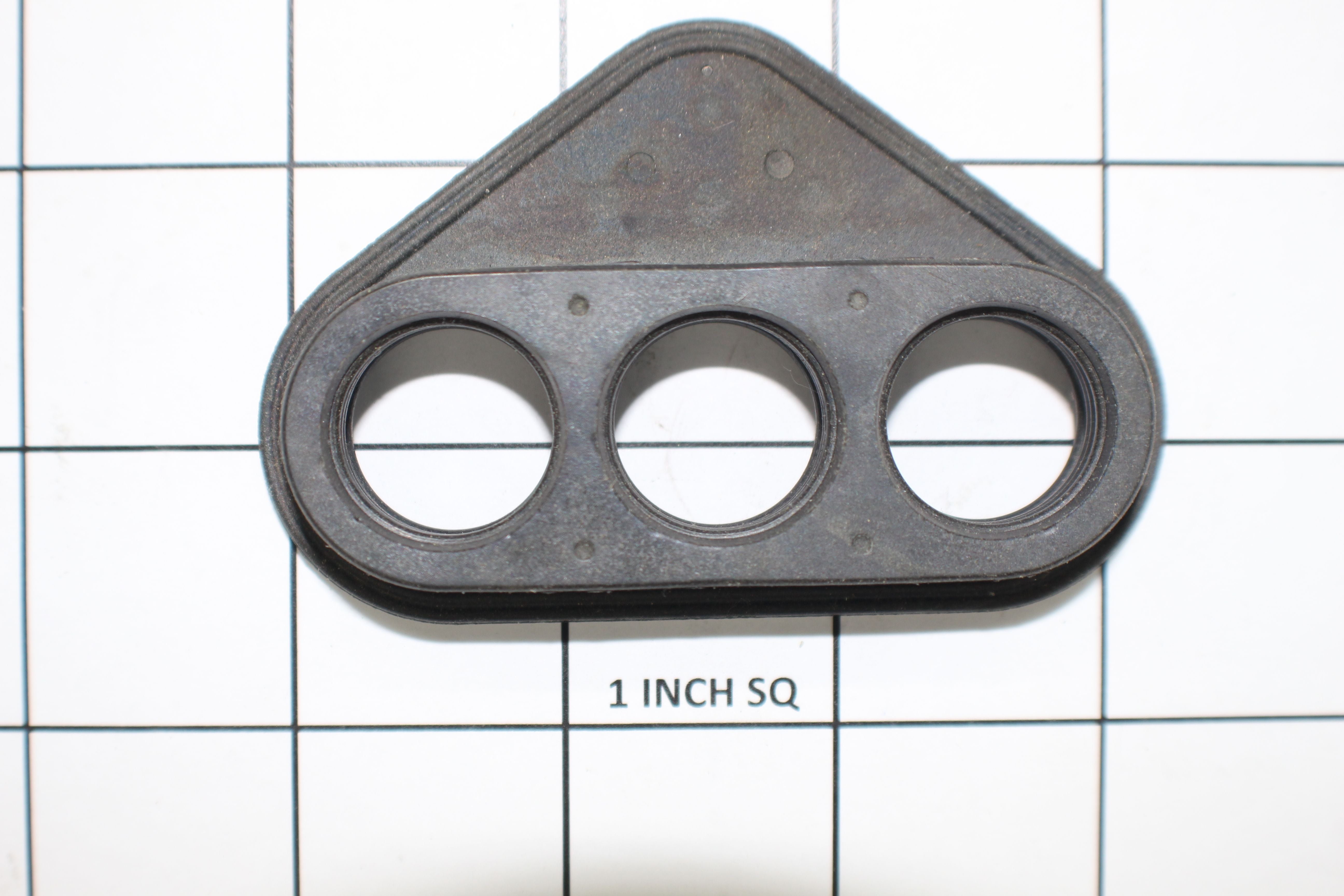 An Indmar Seal for Heat Exchanger, Ford 6.2L—a black, triangular rubber gasket with three holes—rests on a 1-inch grid background, with the gasket centered over three grid squares. Brand: Indmar.