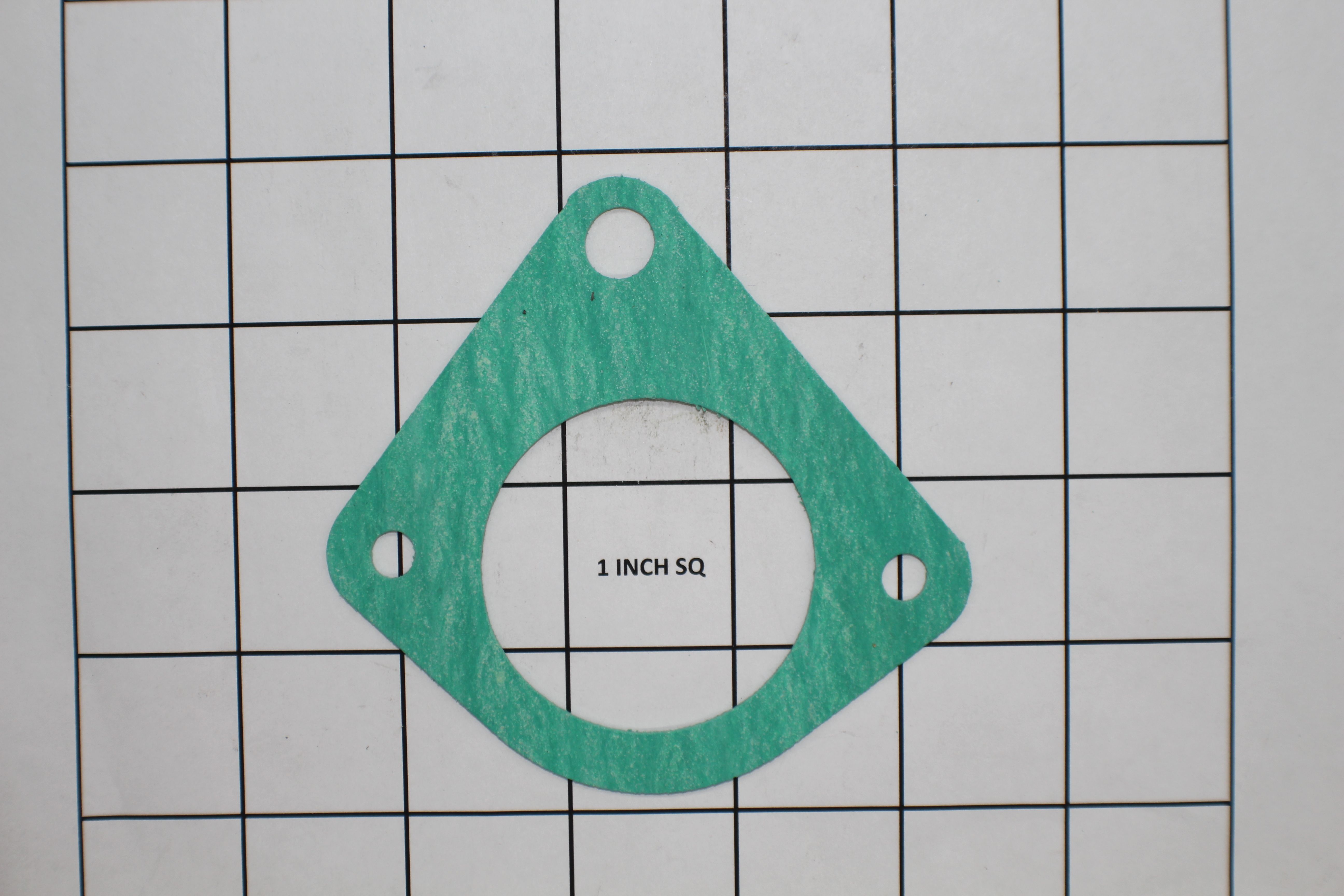 The Indmar LY6 Thermometer Gasket by Indmar, green and triangular with a large center hole and three smaller holes, is shown on a 1-inch grid for scale.