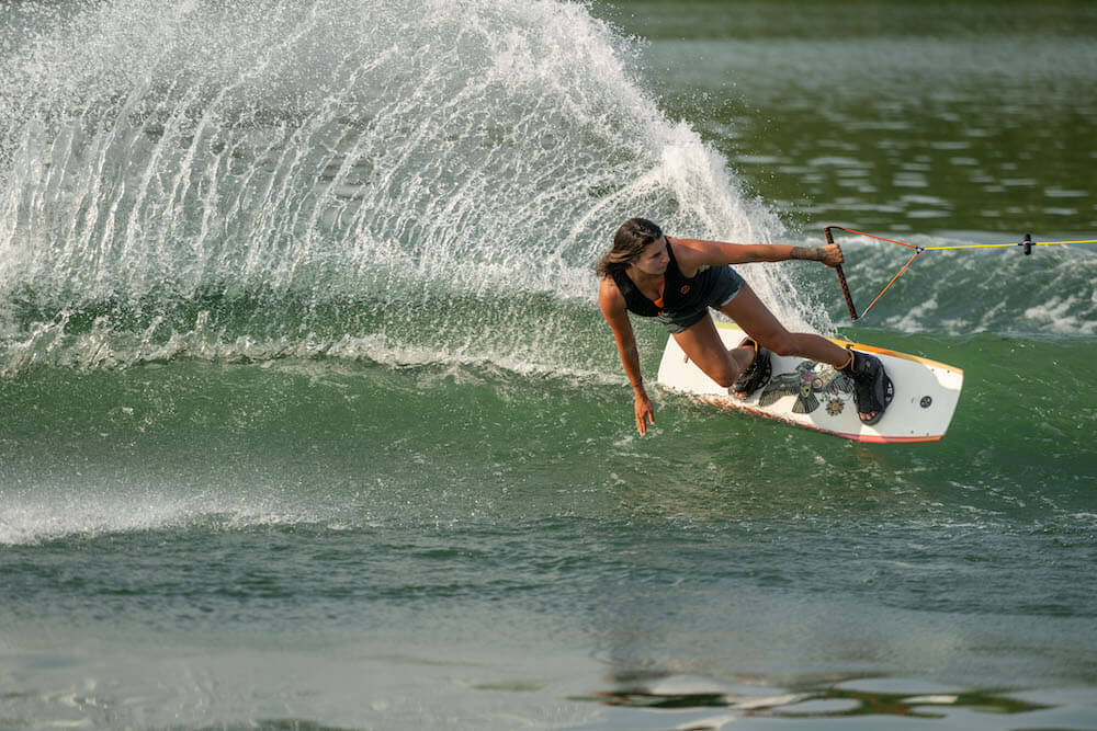 A female athlete is riding a Hyperlite 2024 Cadence Wakeboard in the wake.