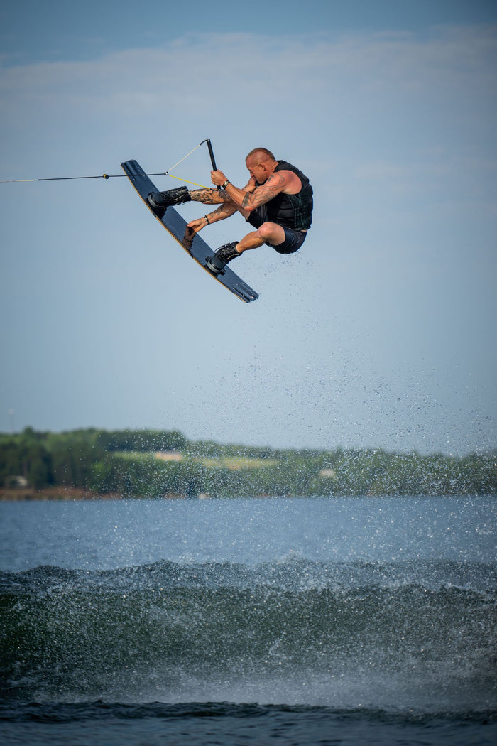 A man is performing a trick on a water ski with the Hyperlite 2023 Rusty Pro Wakeboard and Ultra Bindings.