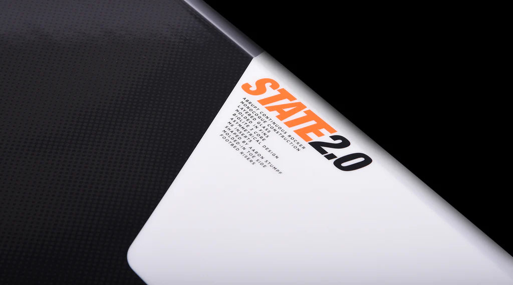 Close-up of a black and white surface featuring the Hyperlite 2025 State Jr Wakeboard with Remix Bindings, along with text in orange and black that likely highlights its asymmetrical design features or specifications crucial for mastering wakeboarding fundamentals.