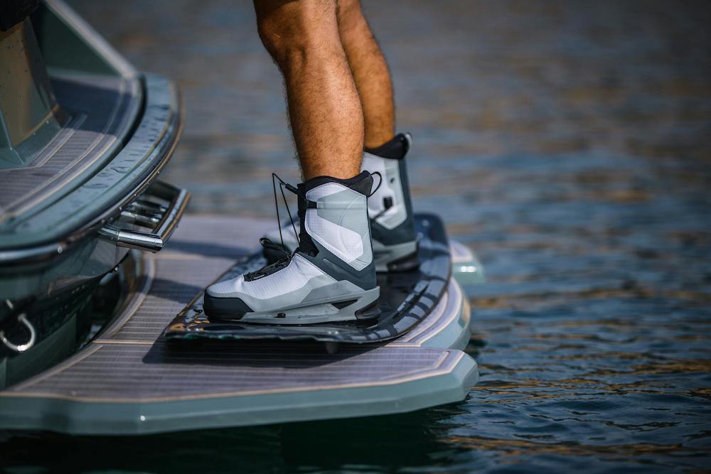 Wearing the Hyperlite Zero02 Boot 2026, a person stands on a boat’s back platform above the water, preparing to wakeboard.