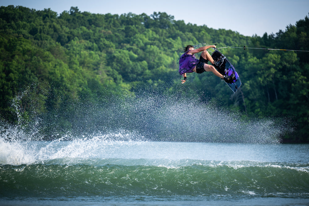 Trever maur wakeboarding on a lake with trees in the background