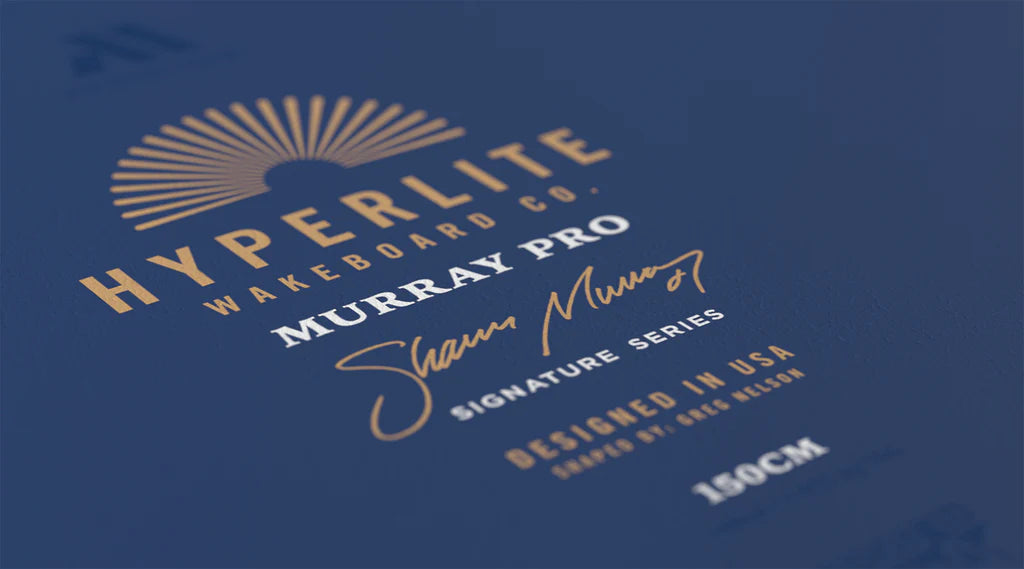 Close-up of the Hyperlite Murray Pro Wakeboard | Team OT Bindings 2026 logo on navy, gold and white text with sunburst graphic, showing Shaun Murray Signature Series, Designed in USA, size 150 cm, and Hyperlite Biolite 3 Core construction.