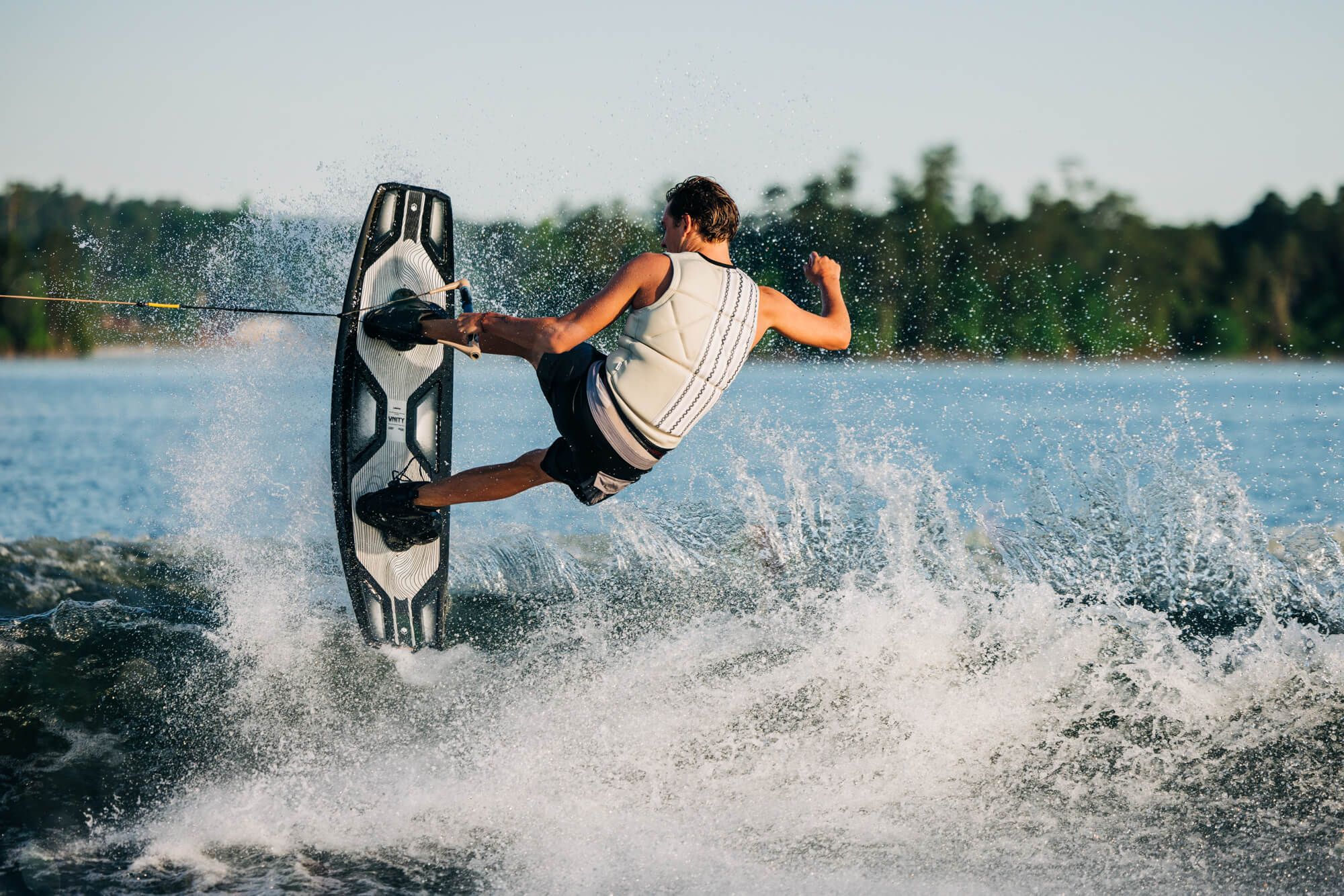 A man showcasing explosive pop while wakeboarding on a lake with the Liquid Force 2024 Unity Aero wakeboard (Pre-Order) featuring an aggressive continuous rocker.