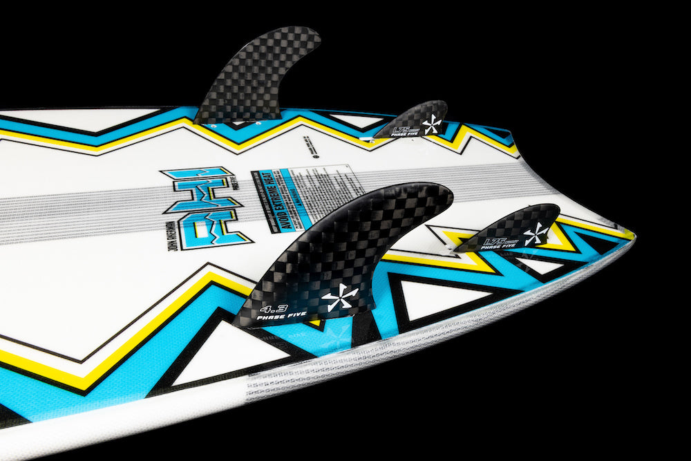 Close-up of the Phase 5 Ahi Wakesurf Board 2026’s tail with three black carbon fiber fins, featuring a bold blue, yellow, black, and white geometric design with visible Phase 5 branding on a black background.