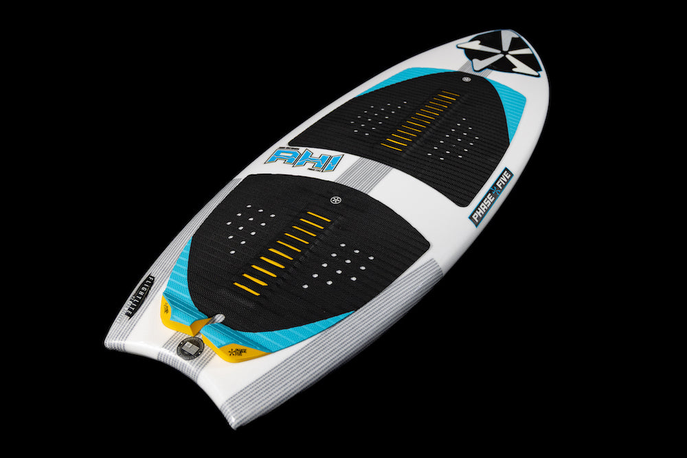 The Phase 5 Ahi Wakesurf Board 2026 is shown on a black background, featuring a white and blue surf design with black grip pads, yellow accents, branding details, a pointed tip, rounded tail, and textured foot areas.