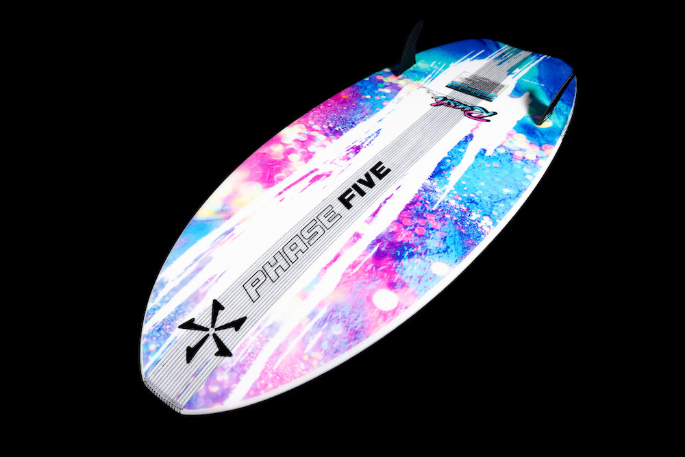 The Phase 5 Rush Wakesurf Board 2026 features bold lettering, a blue, pink, and purple splatter design, and two black fins on a black background—perfect for lightweight performance on the water.