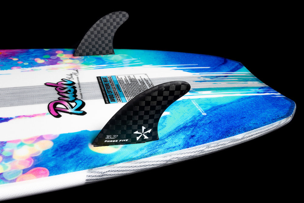 Close-up of the Phase 5 Rush Wakesurf Board 2026 by Phase 5, featuring vibrant blue and white graphics, two black carbon fiber fins, and colorful Rush text—crafted for lightweight performance against a stark black background.