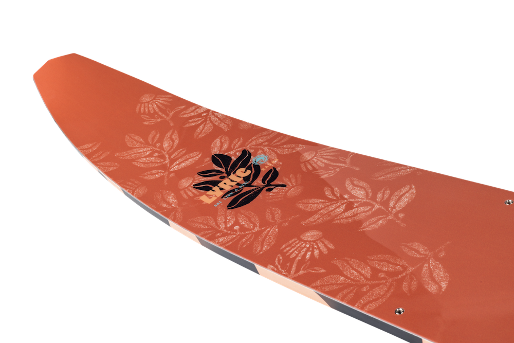 Close-up of the Radar Lyric Women's Waterski | Lyric Boa + Boa ARTP 2026 by Radar, shown in orange with a shiny floral pattern and a central black graphic of a stylized face and leaves, set against a plain white background.
