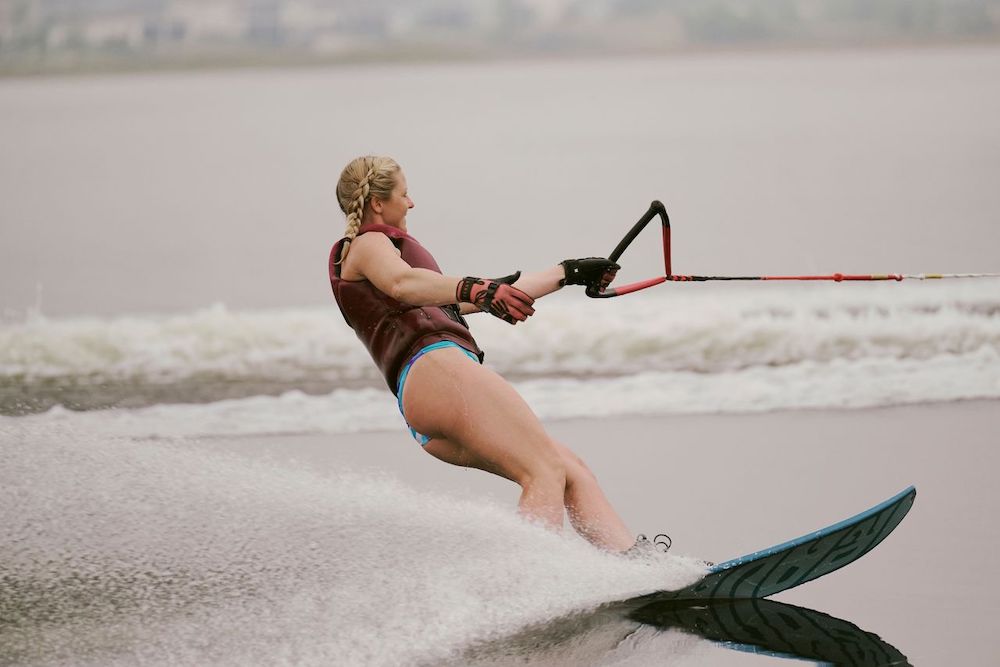 A woman wearing the Radar Session Women's Waterski | Prime + ARTP 2026 by Radar slalom skis on a lake, towing a rope and creating a spray of water behind her.