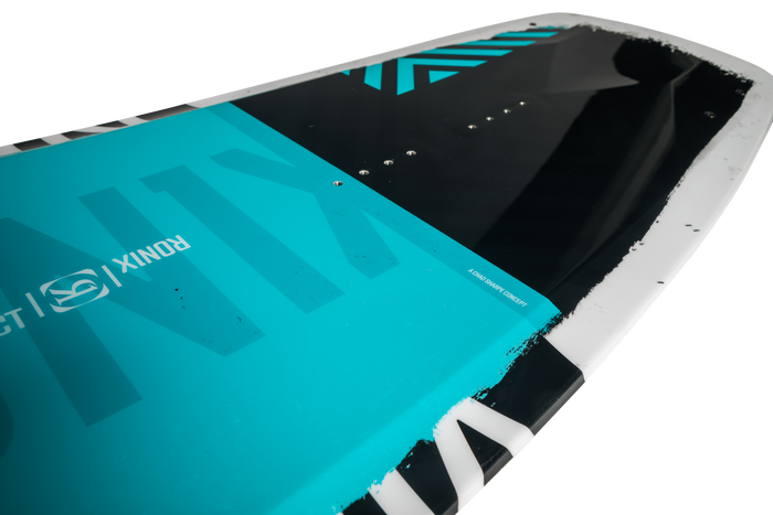 A close-up of the Ronix 2025 District Wakeboard showcases a striking teal, black, and white color design. The brand name Ronix is partially visible, emphasizing the hybrid rocker that allows for explosive jumps.