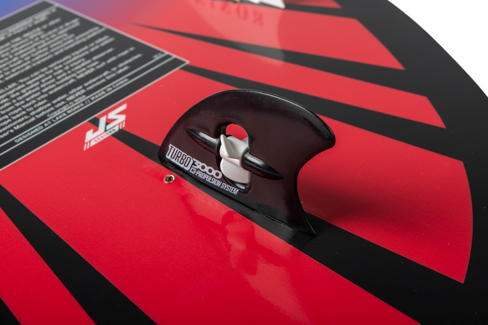 Close-up of the Ronix Sonic Skimmer Wakesurf Board 2026 (3'11"), featuring black fins, bold red and black angular patterns, and a visible section of instructional text in the corner.