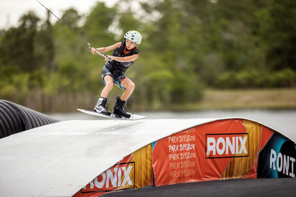 A boy is riding a Ronix Neptune Capella 3.0 Junior CGA Vest on a ramp, showcasing his specific skills.