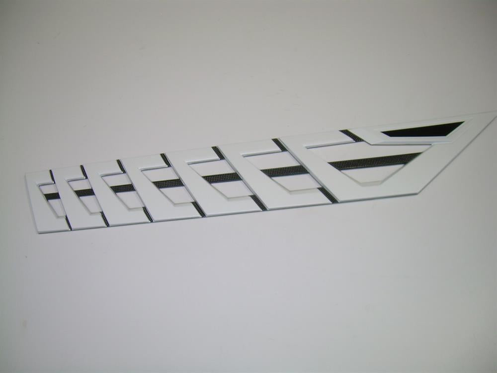 The Nautique DECAL VENT WHITE CHROMAX Starboard 3.85 X 23.59 - 170097 is a white geometric plastic decal with black rectangular insets and slits, resembling a starboard emblem, displayed on a plain white surface.
