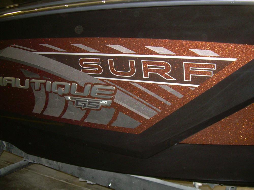 Close-up of a Nautique DECAL SURF HULLSIDE SET PORT & STARBOARD GS20 - 170273, featuring SURF and NAUTIQUE lettering with metallic brown and silver stripes in a glossy finish.