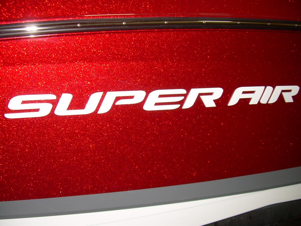 Close-up of a sparkling red metallic surface displaying the Nautique DECAL SUPER AIR WHITE CHROMAX 3" TALL - 170279 by Nautique, likely serving as a bold logo or emblem on a high-performance watercraft.