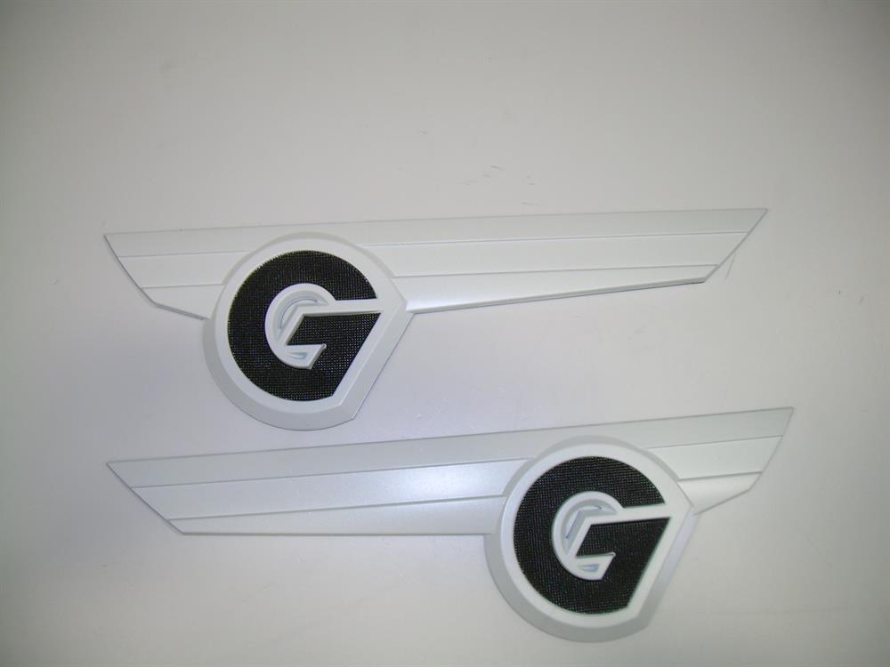 The Nautique DECAL CHROMAX "G" DESIGNATOR WHITE PORT & STARBOARD - 170282 features two identical white plastic boat emblems with a bold white "G" in a black circle, each attached to a wing-like design. Brand: Nautique.