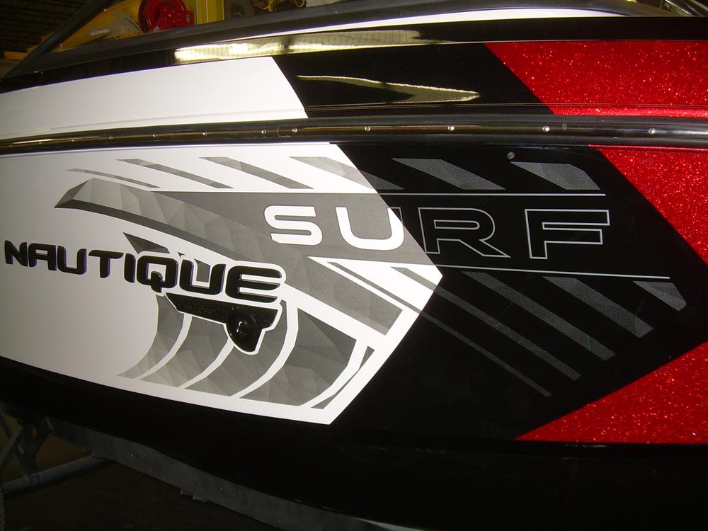 Close-up of the Nautique DECAL SURF GRAPHIC SET PORT & STARBOARD G25 - 170354, highlighting bold Nautique Surf lettering with stylized waves and red, black, and white decal accents on the boat’s side.