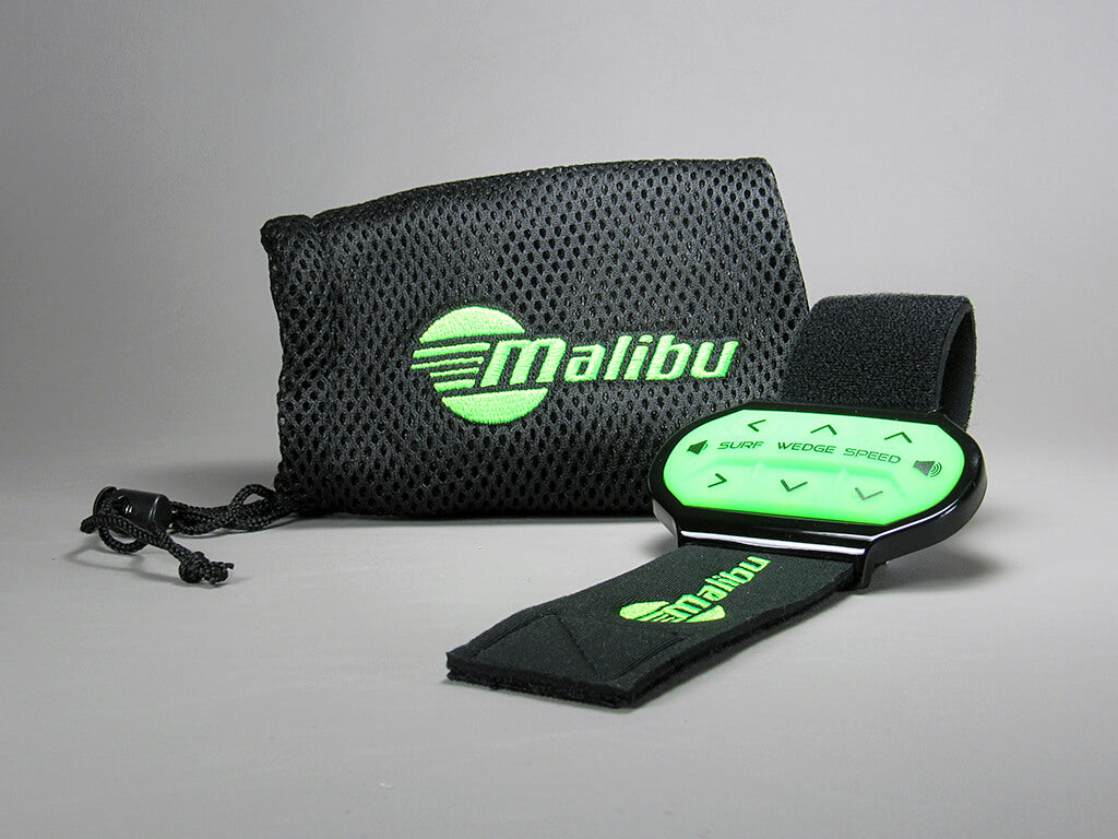 The Malibu Rider Control Wristwatch ('18-) in black and green, featuring labeled buttons, is shown in front of a black mesh carrying pouch on a plain gray background.