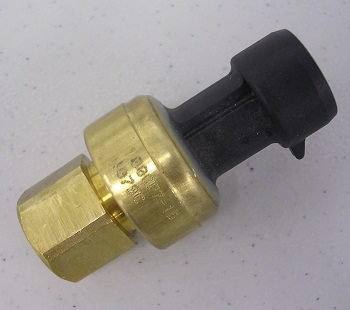 A close-up of an Indmar SENSOR OIL PRESSURE 6.2 FORD - 597013, featuring brass and black plastic, rests on a light speckled surface.
