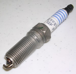 A close-up of an AC Delco Spark Plug Ford 6.2 CYFS-12FP (Set of 16, 597037-16), showing its threaded metal body and white ceramic insulator, designed for Ford 6.2 engines, on a white surface.