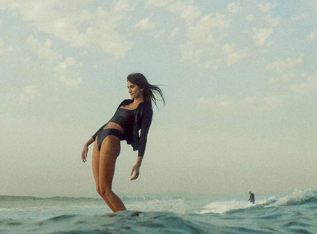 An athlete sporting an O'Neill Bahia Front Zip Jacket wetsuit, confidently balances on top of a surfboard in the vast ocean.