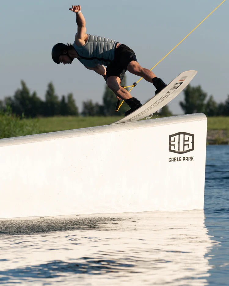 A man is doing a trick on a wakeboard, showcasing maximum flex and impact protection with the Follow 2022 Primary Men's Jacket - Stone from Follow Wake brand.