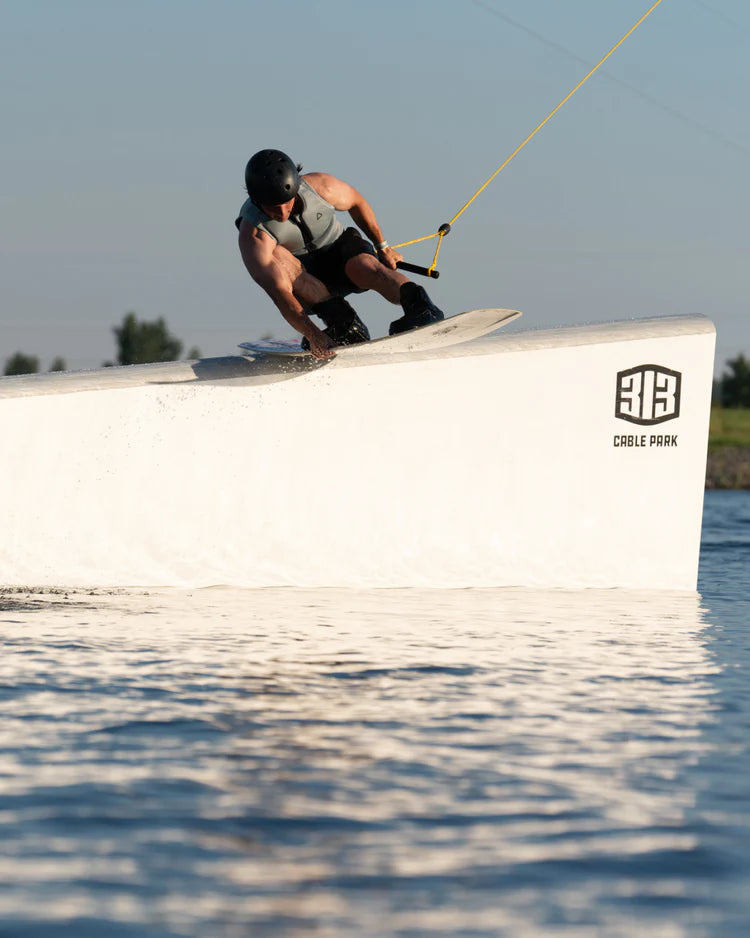 A man is riding a wake board in the water, wearing a Follow 2022 Primary Men's Jacket - Stone from Follow Wake for impact protection and maximum flex.