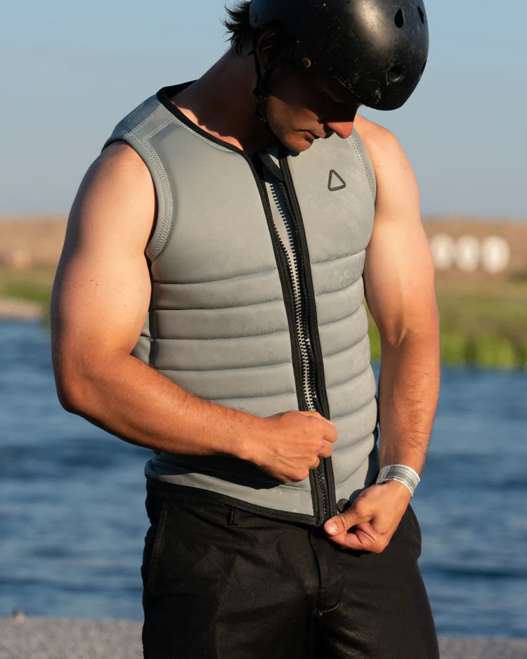 A man wearing a Follow Wake 2022 Primary Men's Jacket - Stone, featuring maximum flex and impact protection, standing next to a body of water.