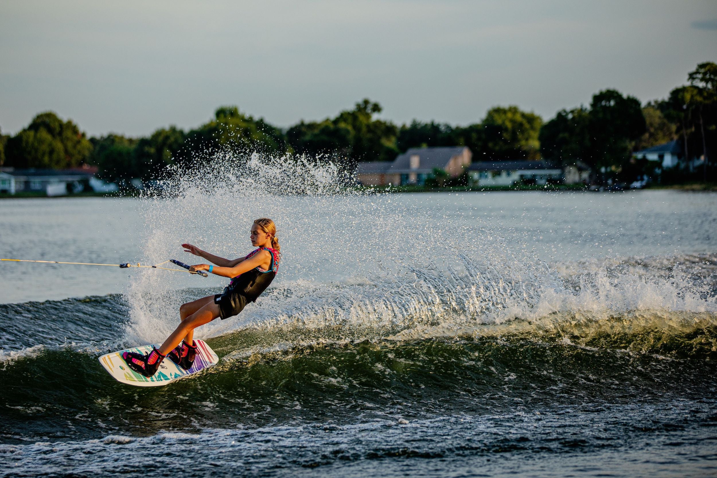 A woman is riding a wave on a Hyperlite 2024 Divine Jr. Wakeboard, showcasing her skills to beginner/intermediate riders.