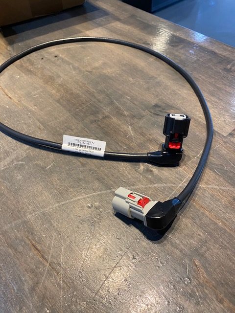 A Malibu Wakesetter '20 Cable Display 1m, 12 to 7 (3962089) with plug n play connectors—one gray, one black with red accents—and a barcode label is shown on a wooden surface.