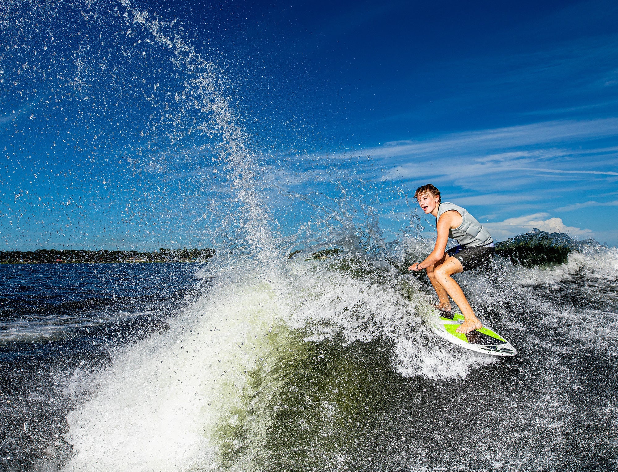 A man seamlessly balancing on a Phase 5 2023 Aku V2 Wakesurf Board as he rides a powerful wave with impressive speed.