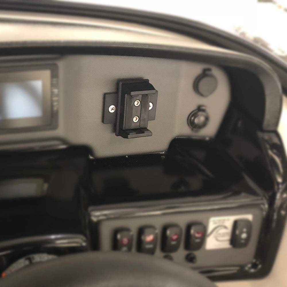 Close-up of a dashboard with the PTM Edge PTM Rotating Phone Holder RPH-100 mounted beside switches, a power outlet, and a small screen, all in a sleek black and gray control panel.