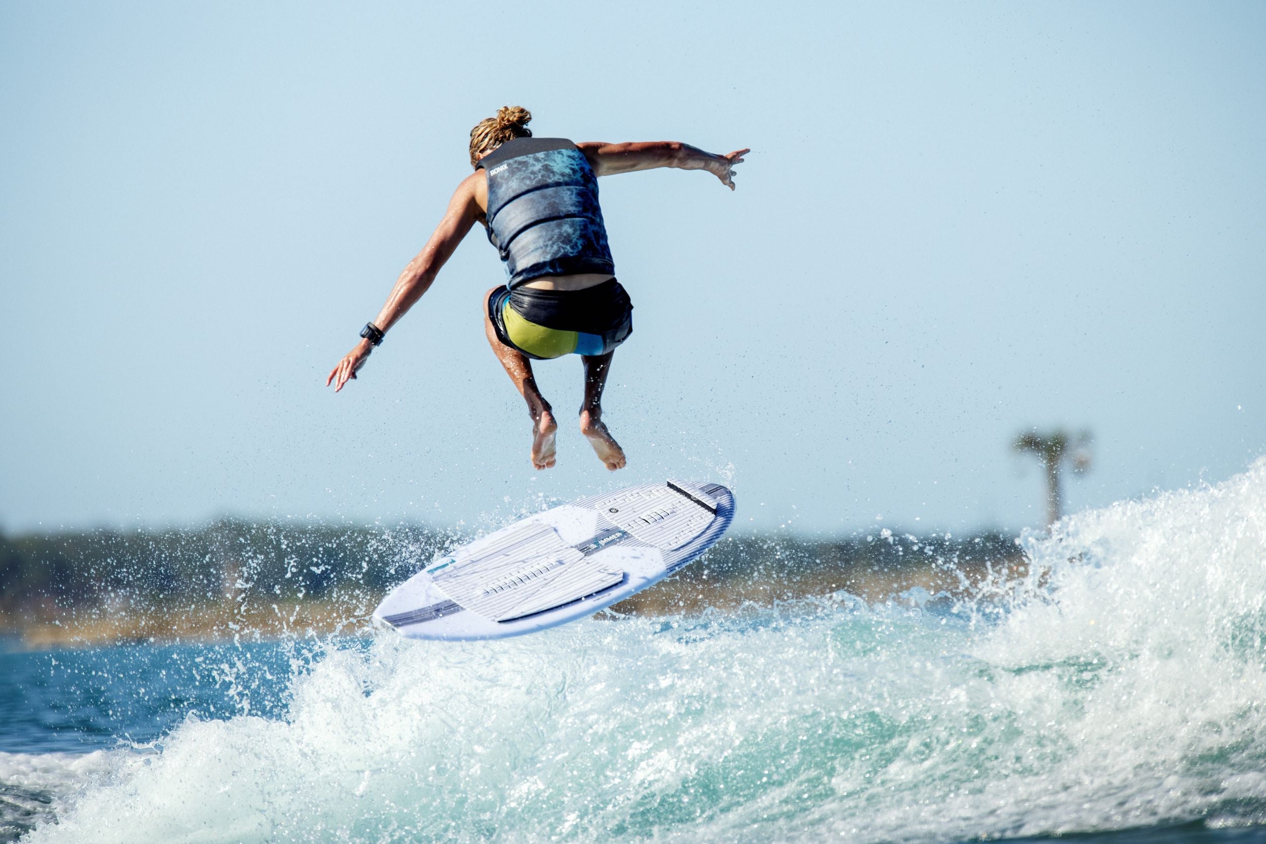 A sea dwelling man is riding a surfboard in the air while wearing a Ronix 2024 Point Break Yes Men's CGA Vest.