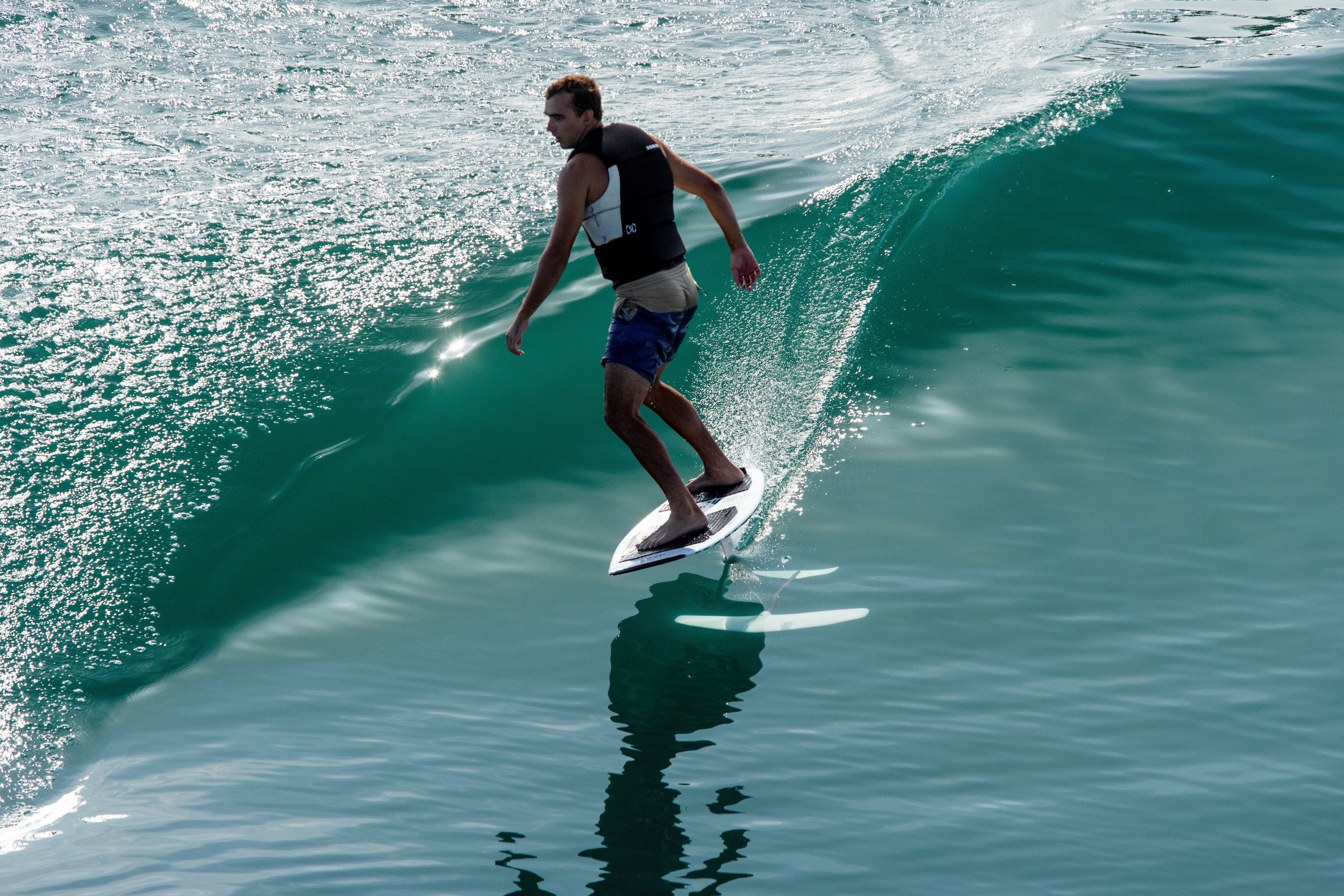 A man riding a wave on a surfboard, showcasing his Ronix 2024 Supreme Yes Men's CGA Vest's supreme buoyancy and mobility.