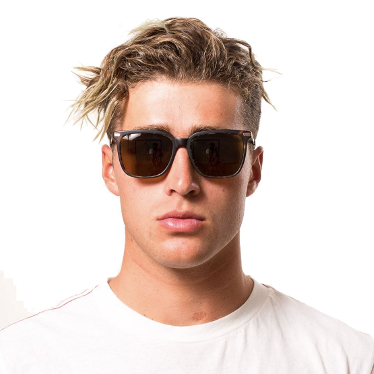 A young person with tousled blonde hair faces forward in a white T-shirt, wearing Otis Crossroads sunglasses in Matte Black/Havana with grey polar lenses, featuring a rounded square frame against a plain white background.