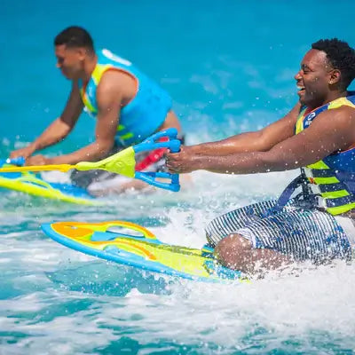 Two men in life jackets ride the ZUP YouGotThis 2.0 Board by ZUP across bright blue water, holding tow ropes and smiling as they enjoy this stable, hydrodynamic beginner water sports board.