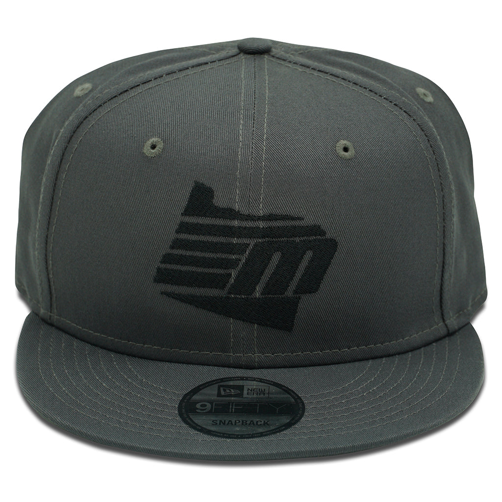 The Malibu Oregon Black/Grey New Era 9Fifty Snapback features a grey cap with a black geometric “M” logo on the front, diagonal lines, a flat brim, and two side ventilation holes.