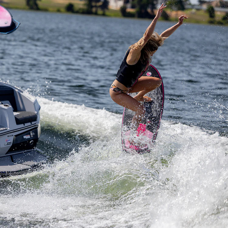 Ashley Kidd wakesurfing on the water next to a Connelly 2024 Carbon AK Wakesurf Board.