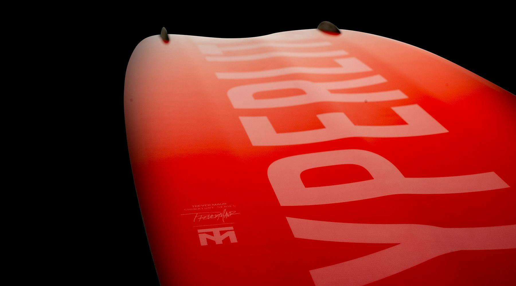 Close-up of a red Hyperlite 2025 Blueprint Wakeboard with large white text, HYPERLITE, on its surface against a black background, promising the softest landing as you pop off the wake.