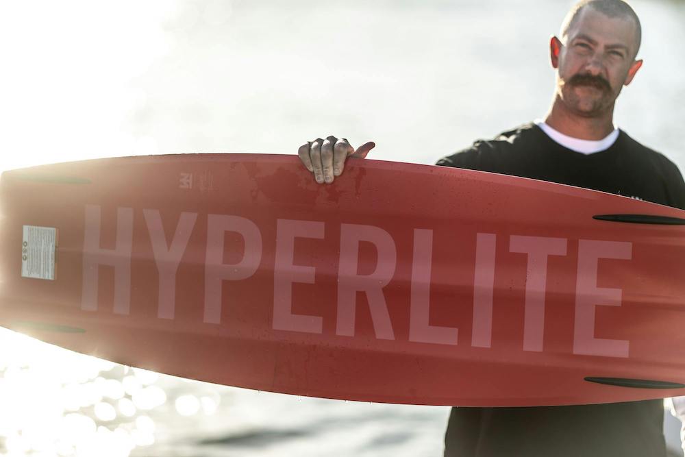 Person holding a Hyperlite 2025 Blueprint Wakeboard near a body of water, preparing to launch off the wake with what is known to be the softest landing board.