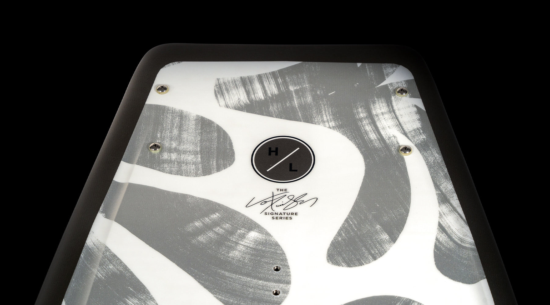 A close-up of a snowboard showcases a black and white abstract pattern, highlighted by a circular logo displaying "HL" with a signature beneath it on a black border. This design evokes the sleek aesthetic characteristic of the Hyperlite 2025 Capitol Wakeboard, seamlessly blending style with performance.