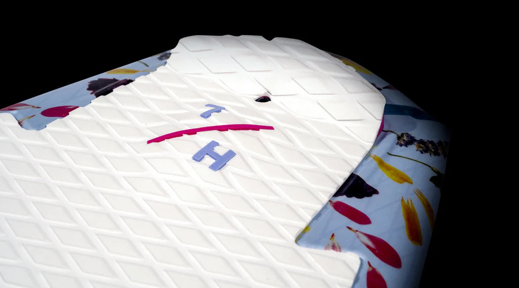 Close-up of a textured white surface with a colorful floral background, showcasing the letters T and H next to a small hole, reminiscent of the vibrant world of wakesurf enthusiasts using the Hyperlite 2025 Good Daze Women's Wakesurf Board.