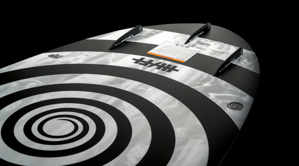 Displayed against a black background is the Hyperlite 2025 Hi-Fi Wakesurf Board, showcasing a striking black and white spiral and stripe design. It features DuraShell construction with an EVA traction pad and three fins on the underside, providing exceptional grip to enhance its skim style performance.