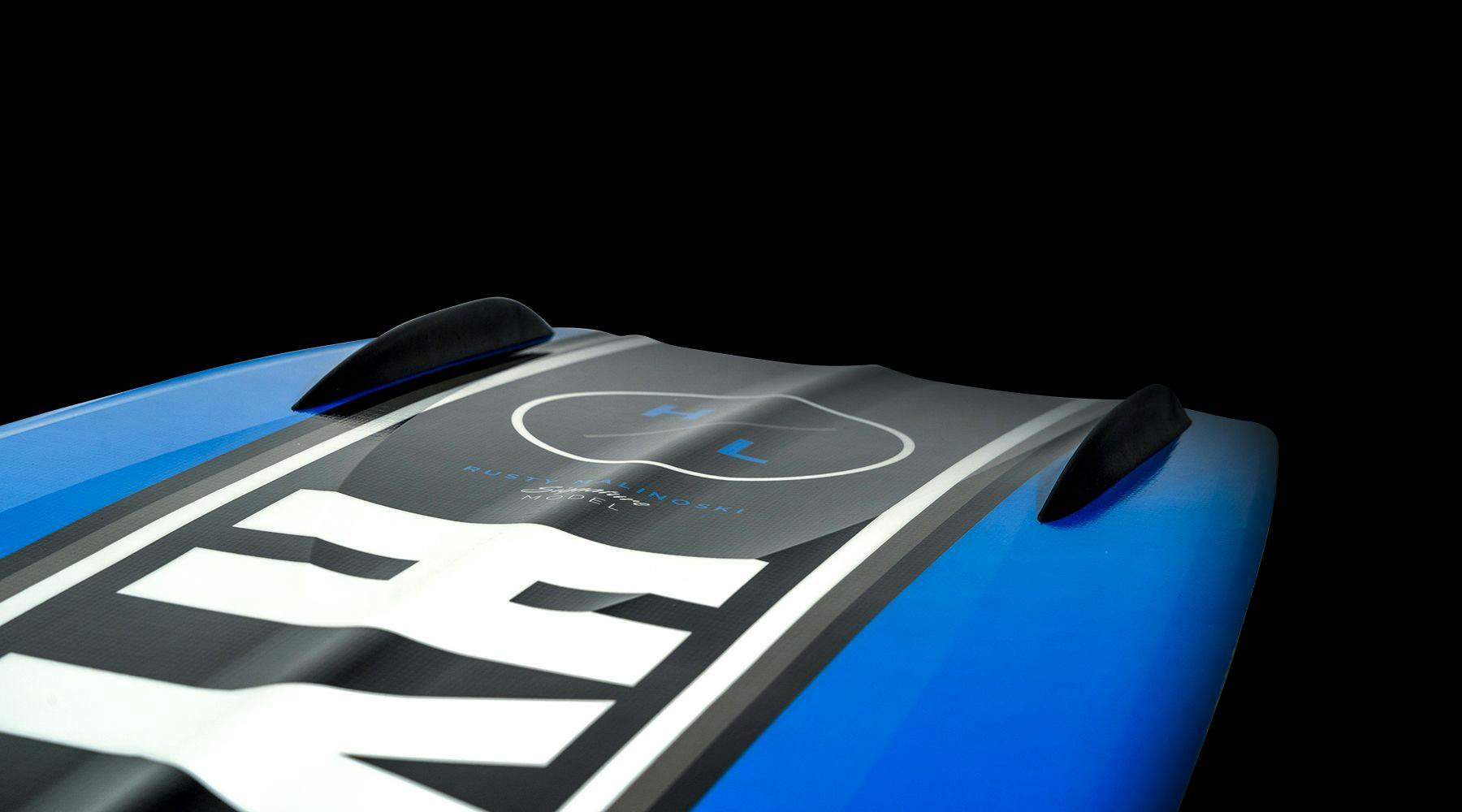 Close-up of a blue Hyperlite 2025 Kruzr-GLS Wakeboard set against a black background, highlighting the white Hyperlite logo and the detailed fins along its cupped tail rail.