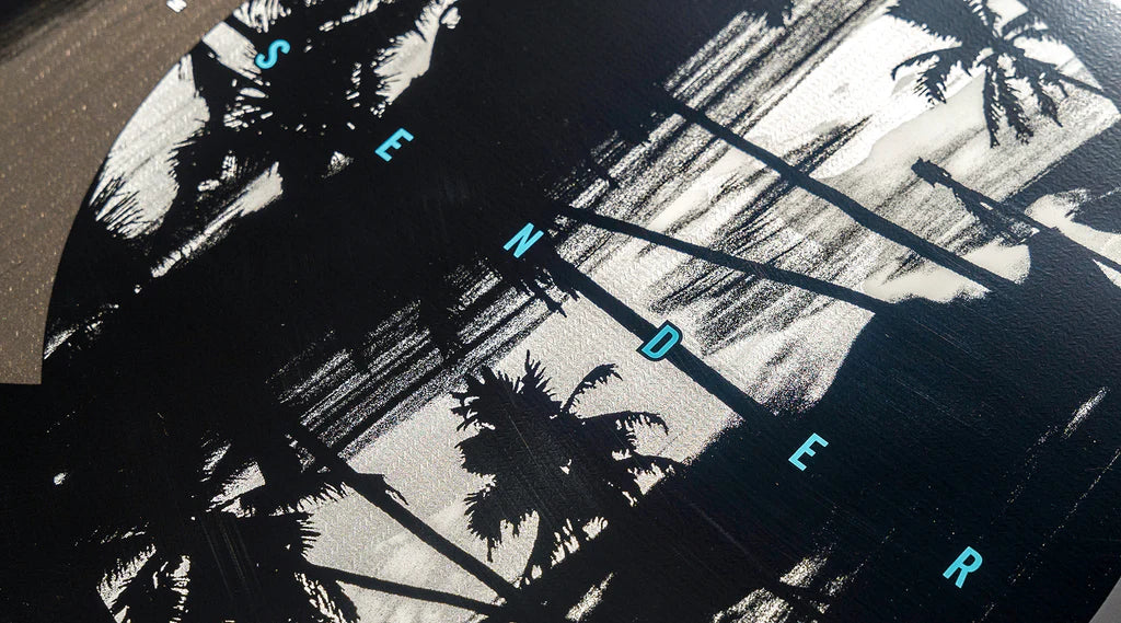 Close-up of the Hyperlite 2025 Sender Wakeboard showcasing the word "SENDER" in blue letters against a black and white palm tree silhouette, evoking the stylish design of a wakeboard, all set against a circular background.