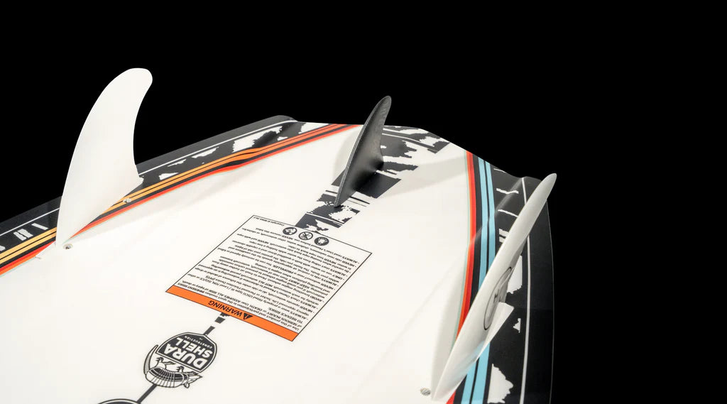 Close-up of the Hyperlite 2025 Shim Wakesurf Board bottom showcasing three fins, a colorful striped design, and a warning label. This board boasts SHIM technology and DuraShell Construction for enhanced durability, ideal for a versatile crossover design that performs well in diverse wave conditions.